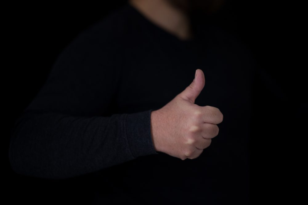 A man in a dark suit with his thumb up